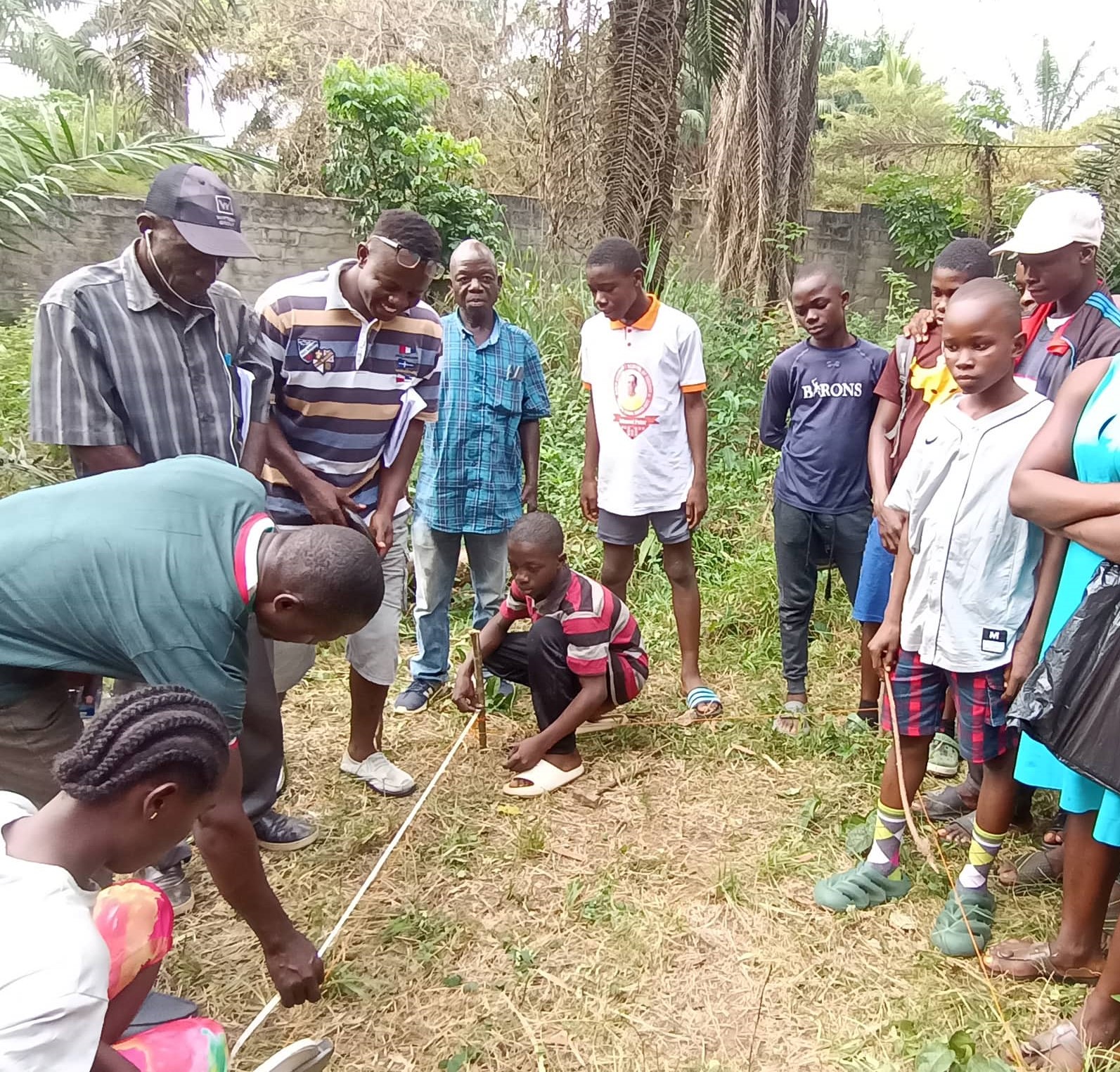 John Kucuyoiyoigee one of our trainers, is teaching the students how to measure out the garden beds. Preston Gonmiah is their Agriculture Teacher. He is in the orange striped T-shirt. Preston was honored with a Thrive Institute Scholarship.