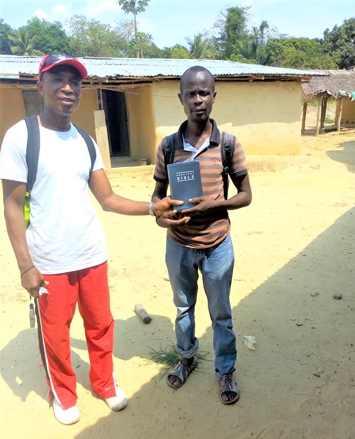 Pastor Malcolm is handing a Bible to a Leader in a remote village.